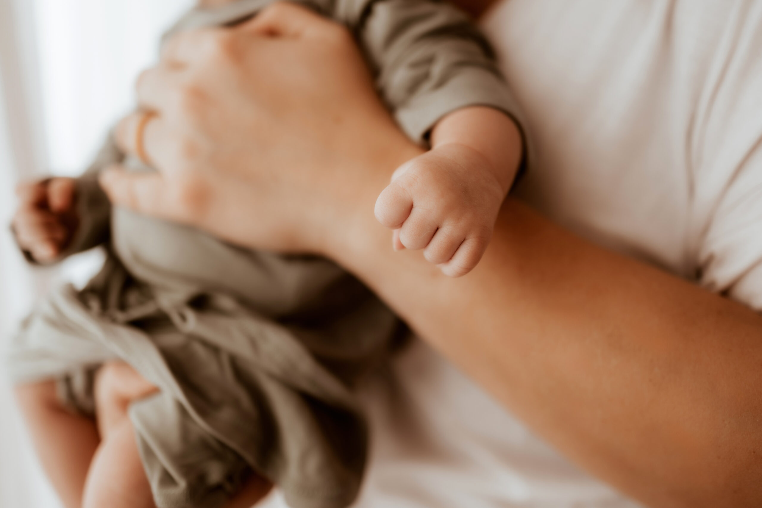 Detail photo of newborn baby girl hands wearing a sage green sleeper sack