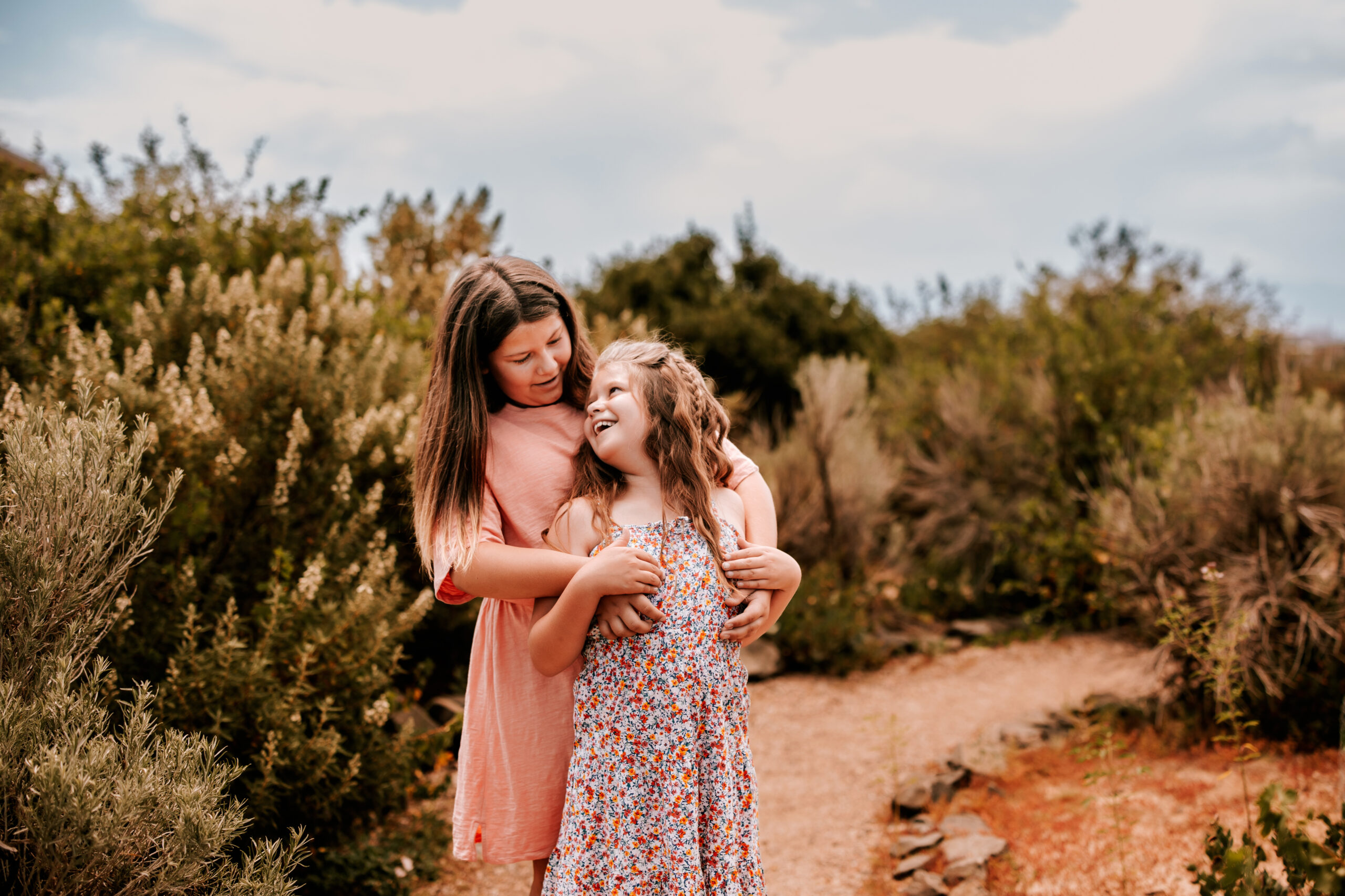 Sisters hug in front of pretty flowers for a summer family photo session in Colorado