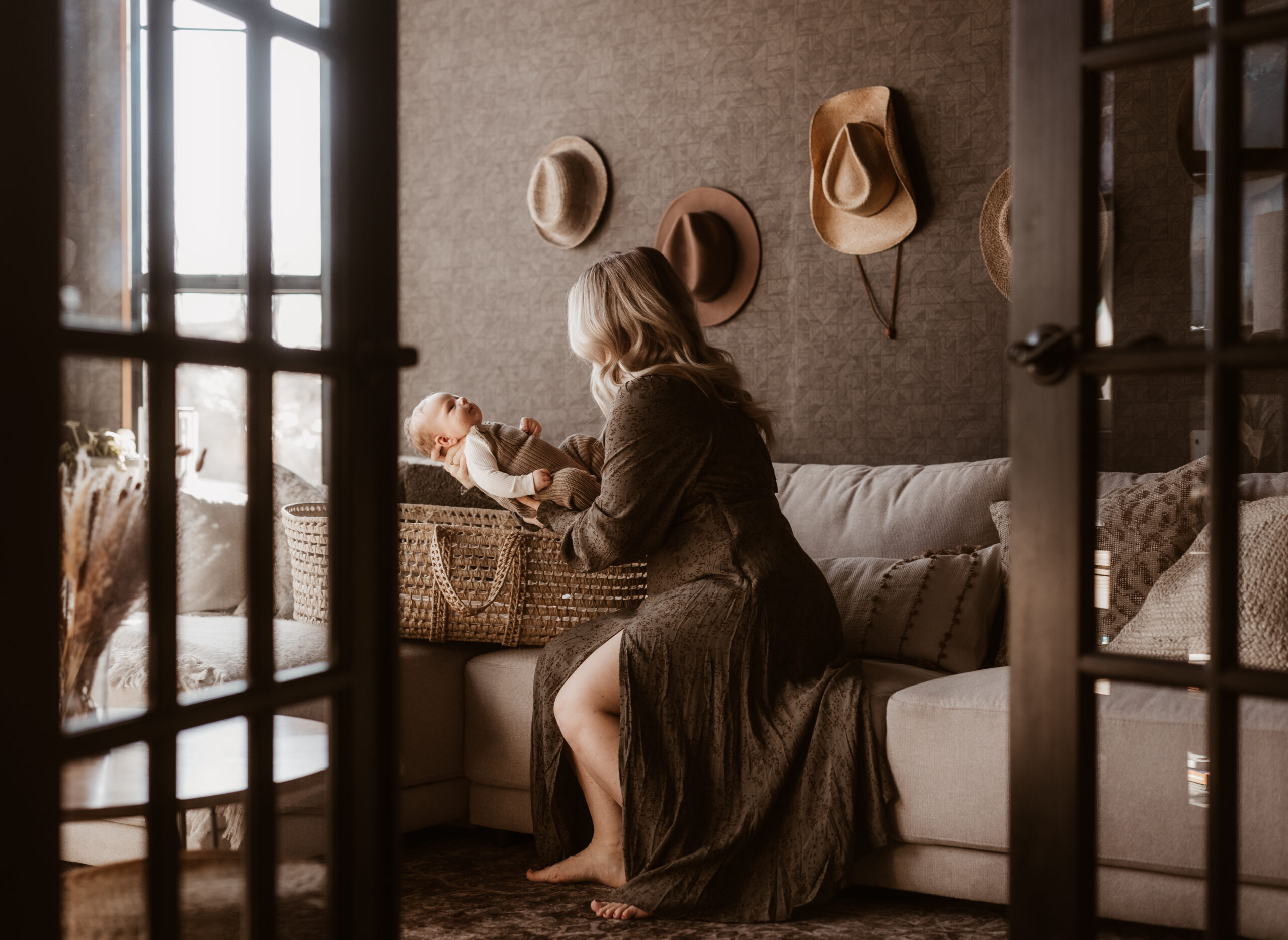 mom in dress places newborn baby in basket in living room